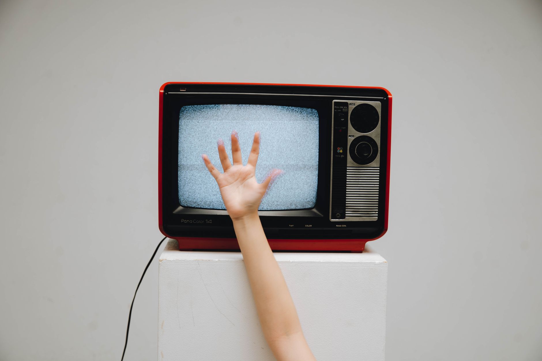 A classic retro television displaying static with a hand reaching towards the screen.