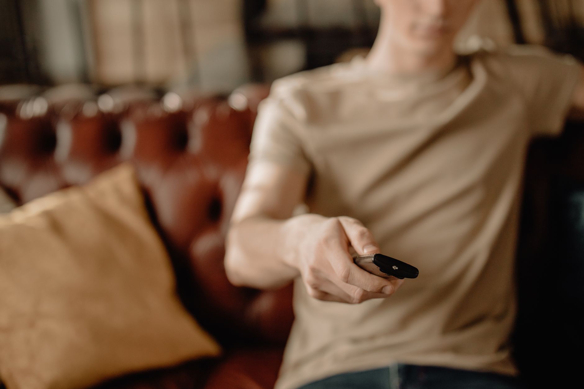Person relaxing on a leather sofa at home, holding a remote control. Cozy and casual atmosphere.