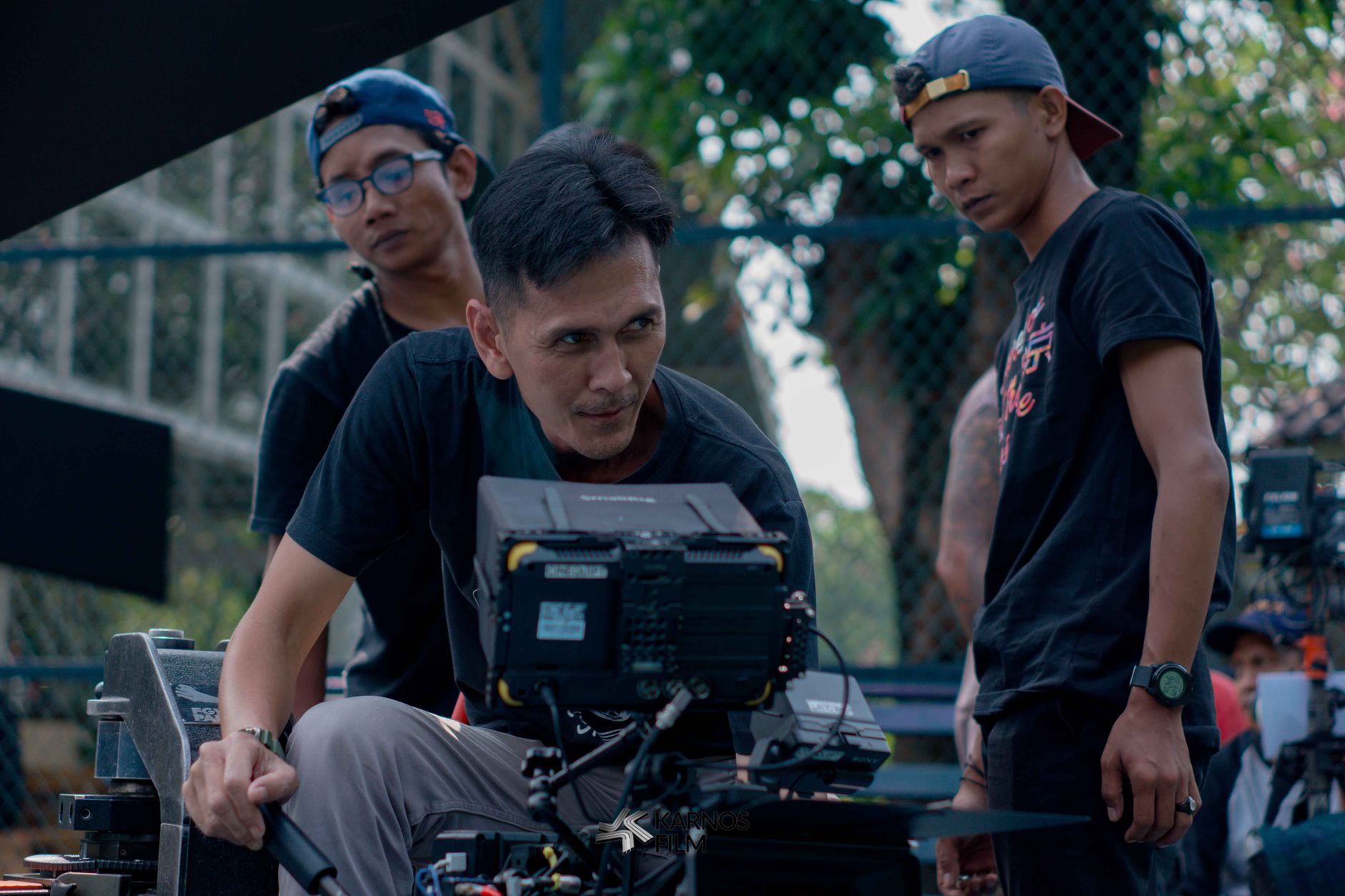Group of filmmakers reviewing footage on set outdoors, focused on camera equipment.