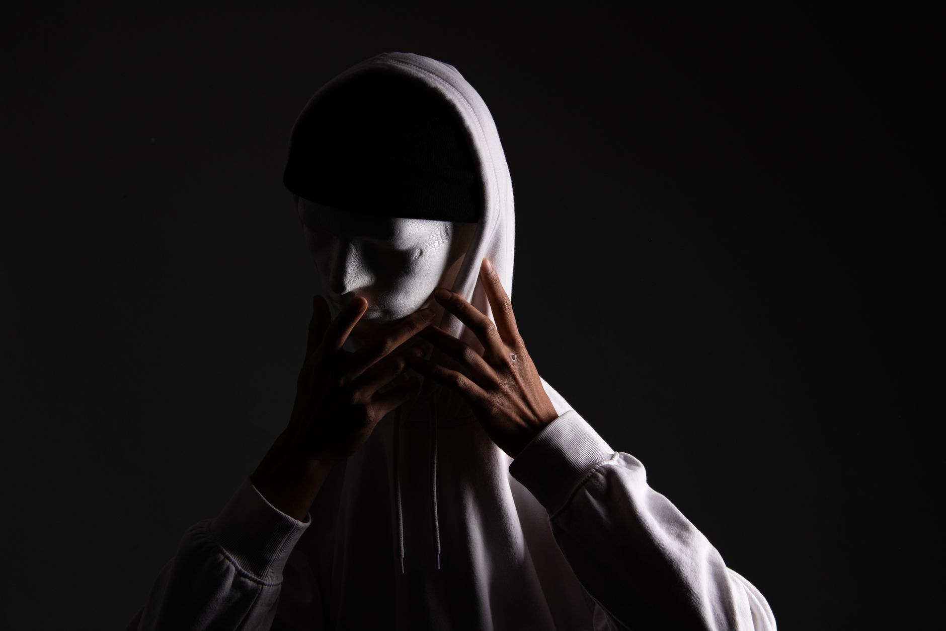 A dramatic image of a person wearing a mask and hoodie, casting a mysterious vibe.