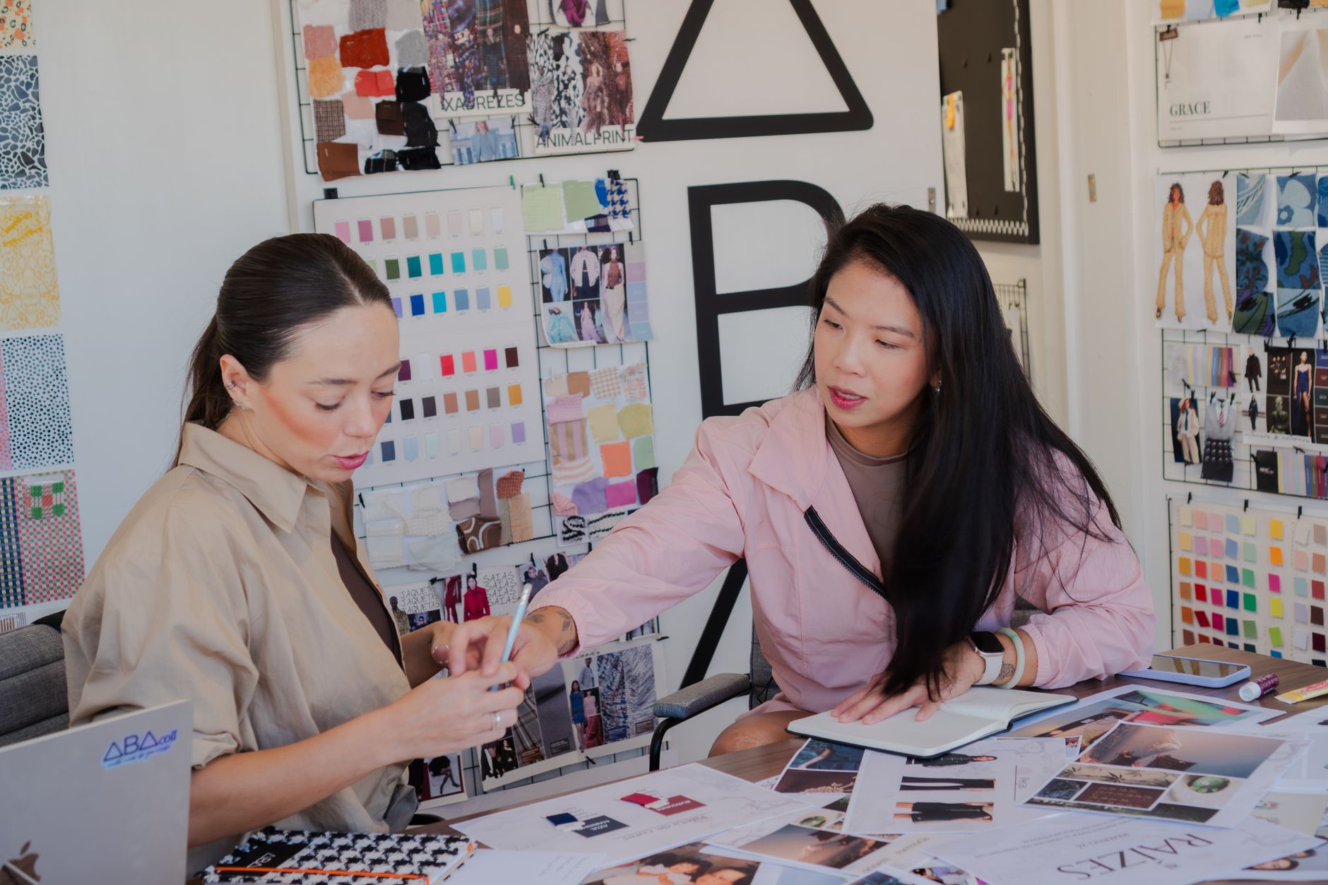 Two fashion designers in a studio collaborating on a design project, surrounded by fabric swatches and sketches.