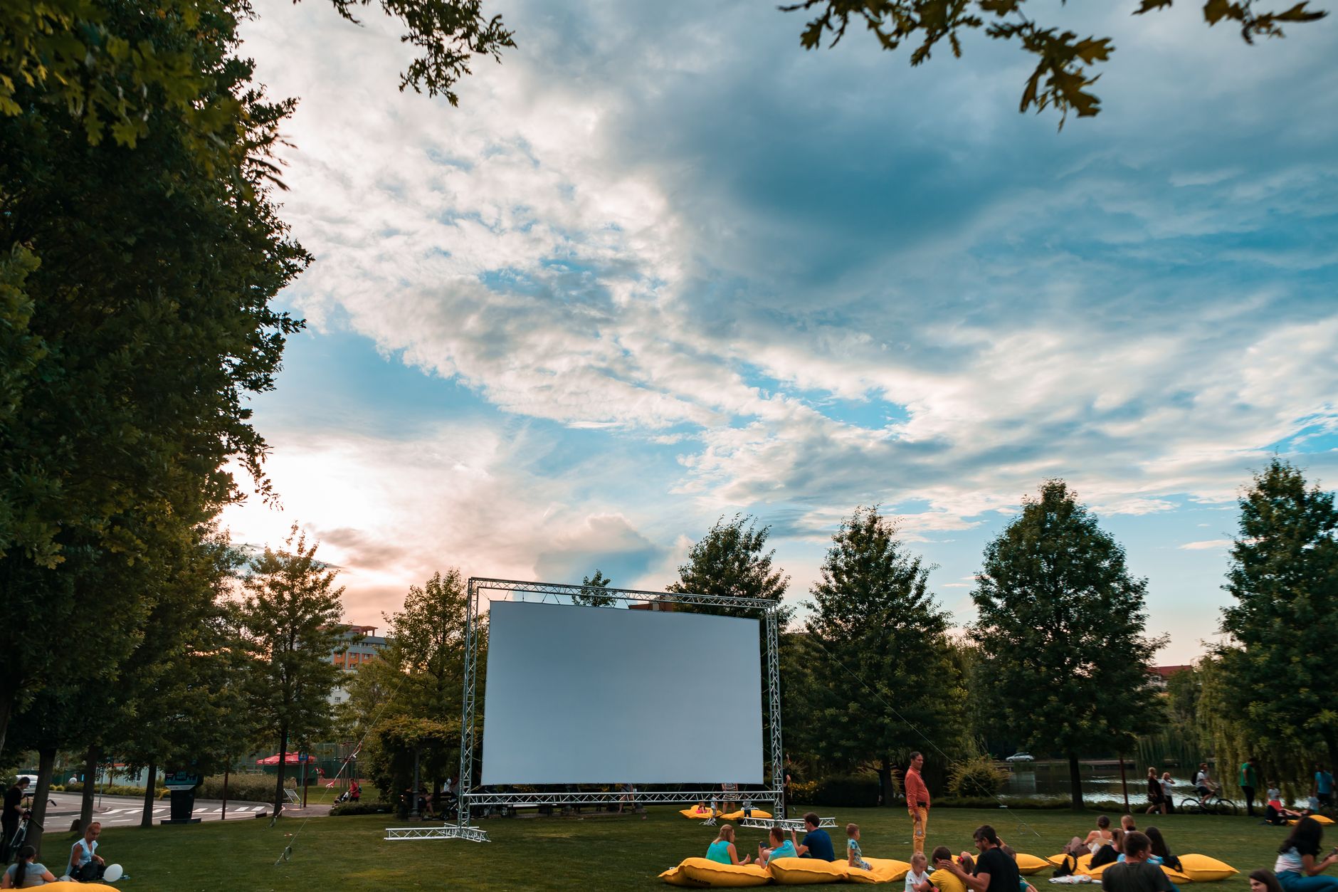 Grand écran de cinéma en plein air installé sur une pelouse entourée d’arbres face à des spectateurs.