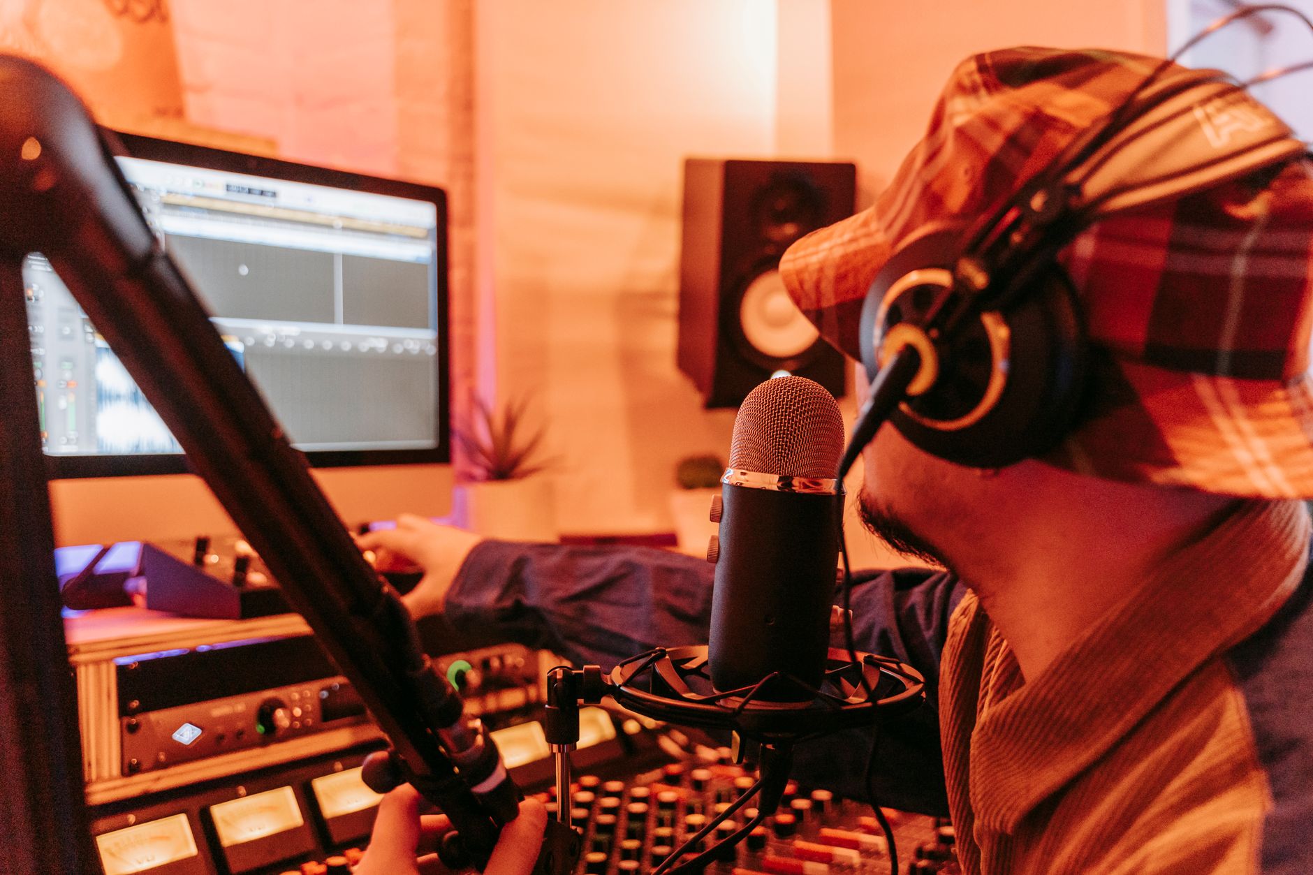 Personne casquée devant un micro dans un studio d’enregistrement, avec table de mixage, écran audio et enceinte.