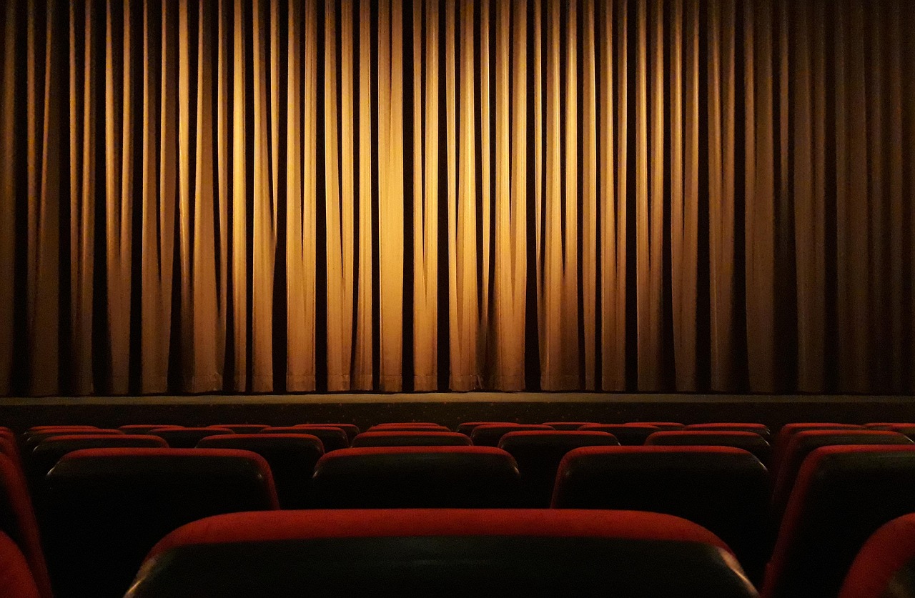 Rideau de scène couleur or devant des rangées de sièges rouges vides dans une salle de spectacle.